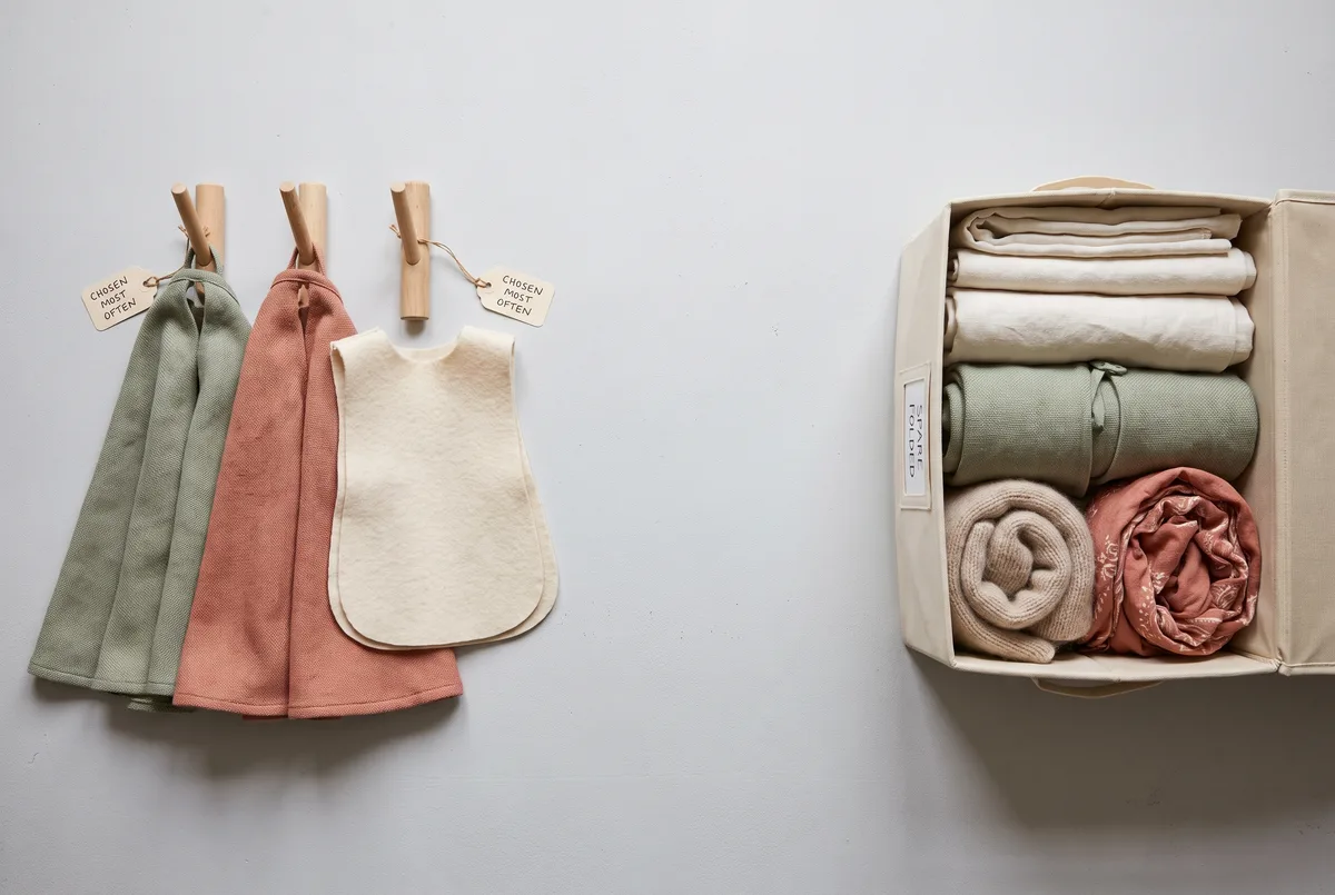 An overhead sorting comparison: on the left two capes and a tabard laid out ready to hang on wooden pegs; on the right lengths of fabric, a spare cape, a soft prop and a scarf folded into a shallow open canvas bin.